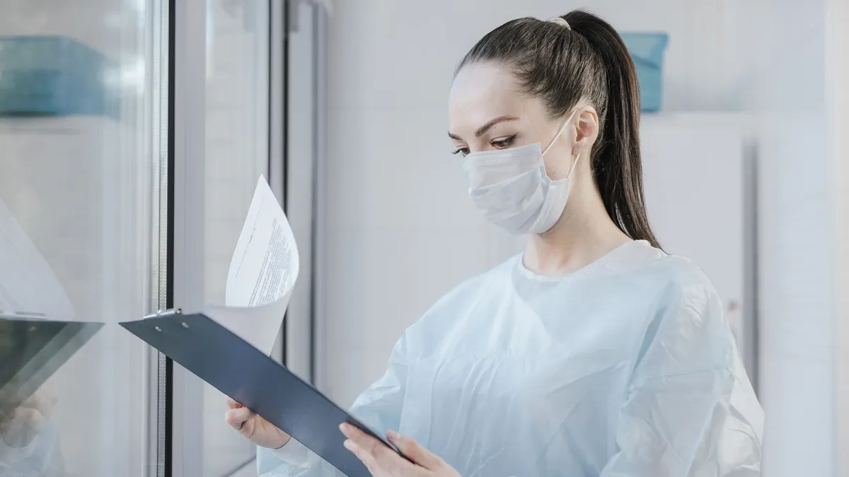 A female doctor in a mask examining patient's medical records in a hospital setting.
