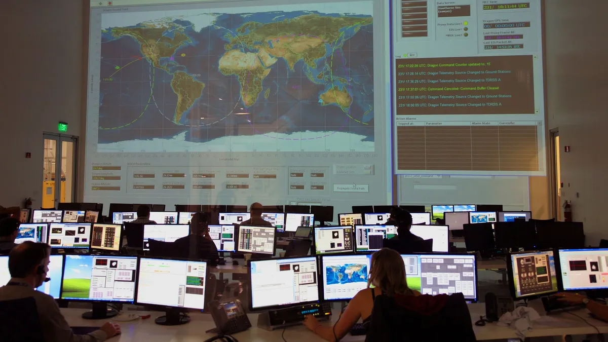 Back view of unrecognizable employees working on computers in flight control room with big interactive map on wall and analyzing data