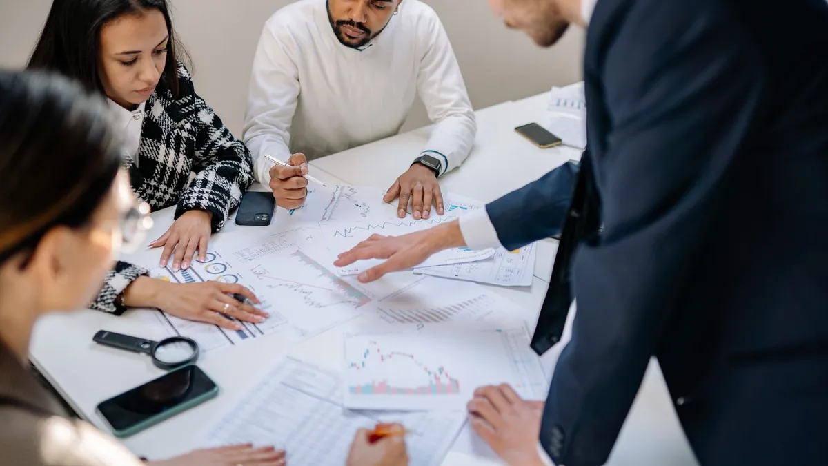 A diverse team collaborating in an office meeting, discussing papers with charts.