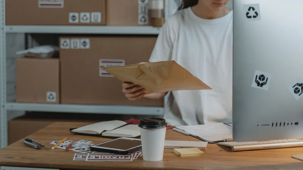 Woman sorting parcels at her desk in a logistics office, demonstrating efficient workspace organization.