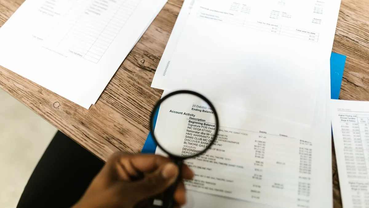 Close-up of hand using magnifying glass to review documents. Ideal for financial themes.