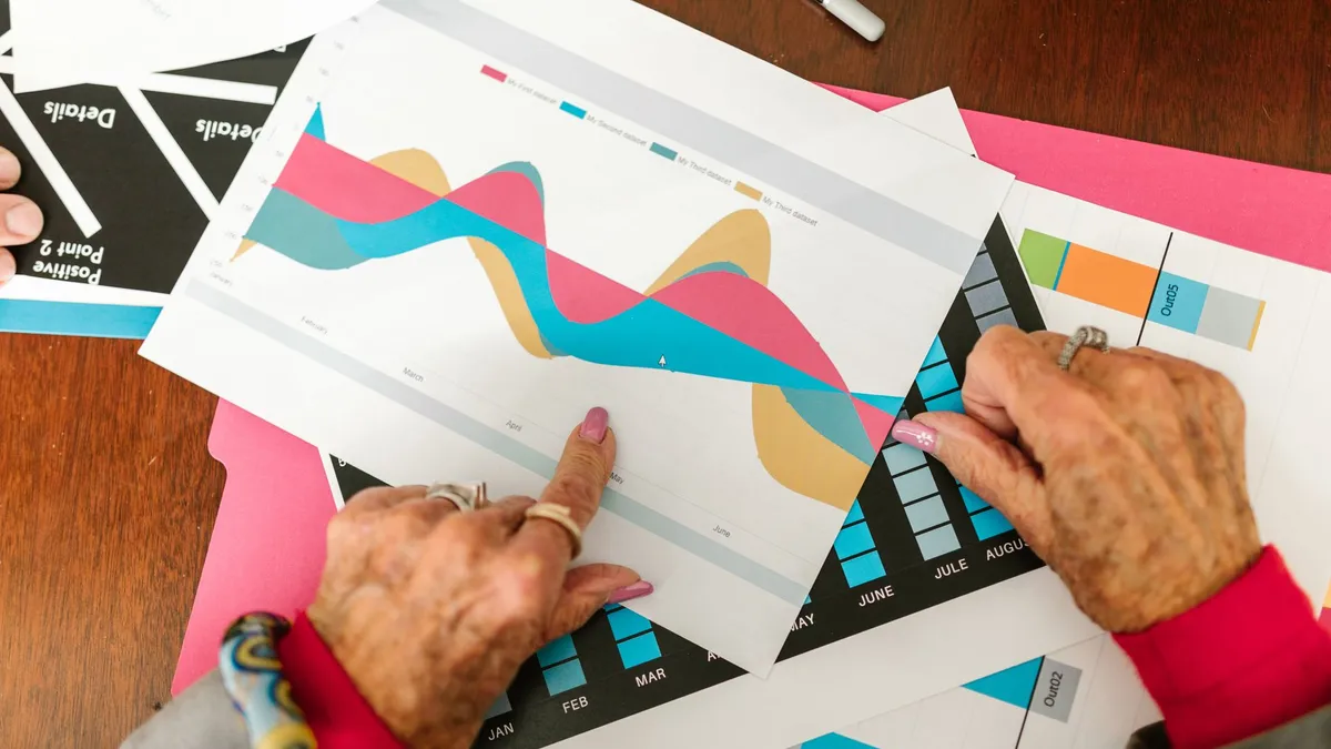 Senior adult pointing at colorful business graphs with data analysis documents on a wooden table.