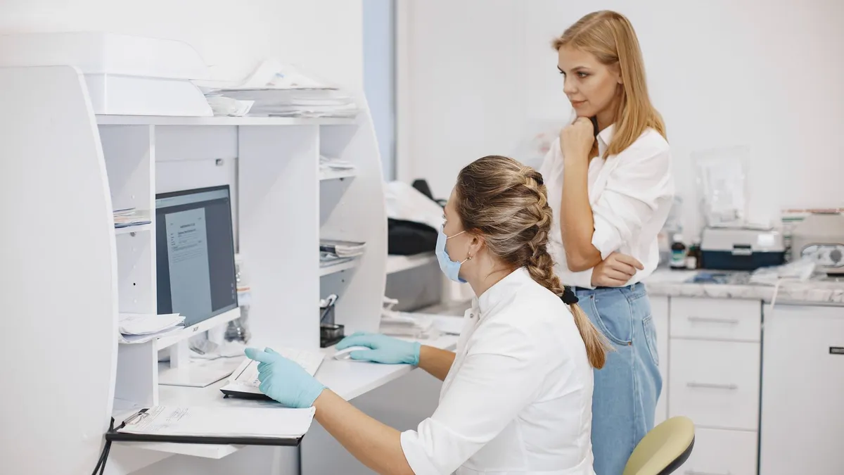 Two female healthcare workers in a clinical office, reviewing diagnostic results on a computer screen.