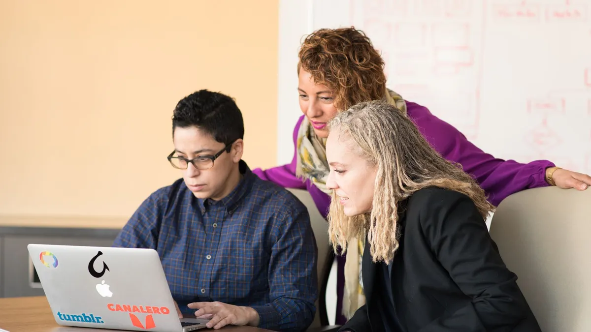 Team of three people collaborating on a laptop in an office setting.