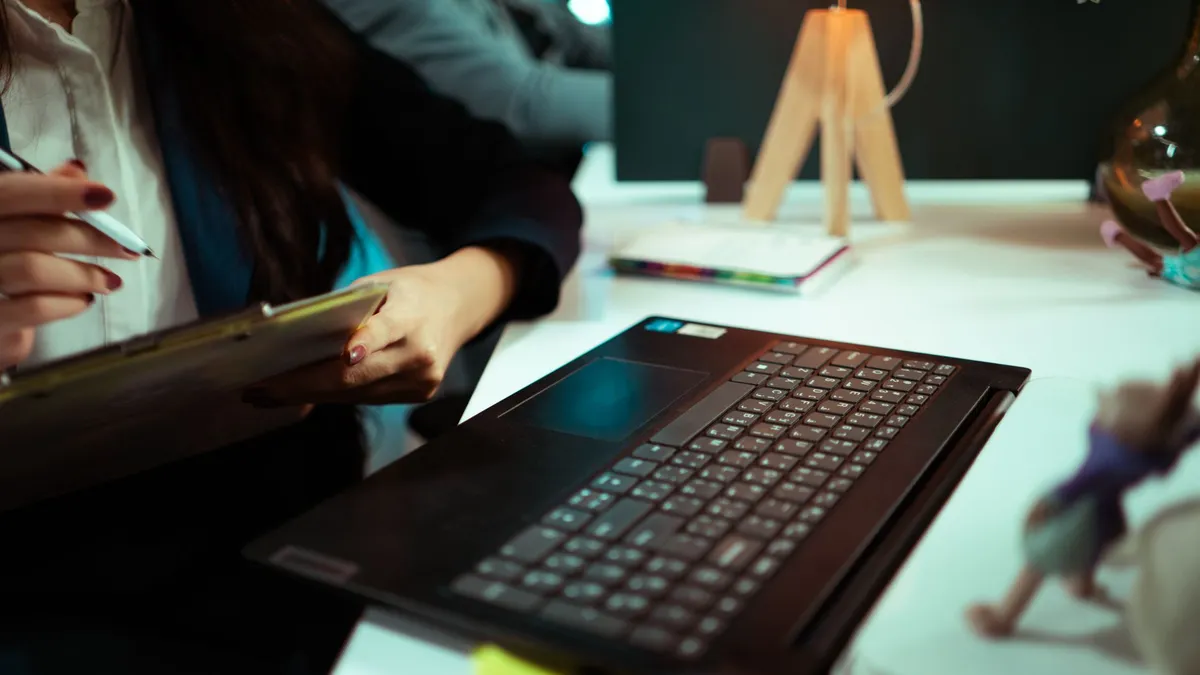 Businesswoman taking notes while working on a laptop in an office.