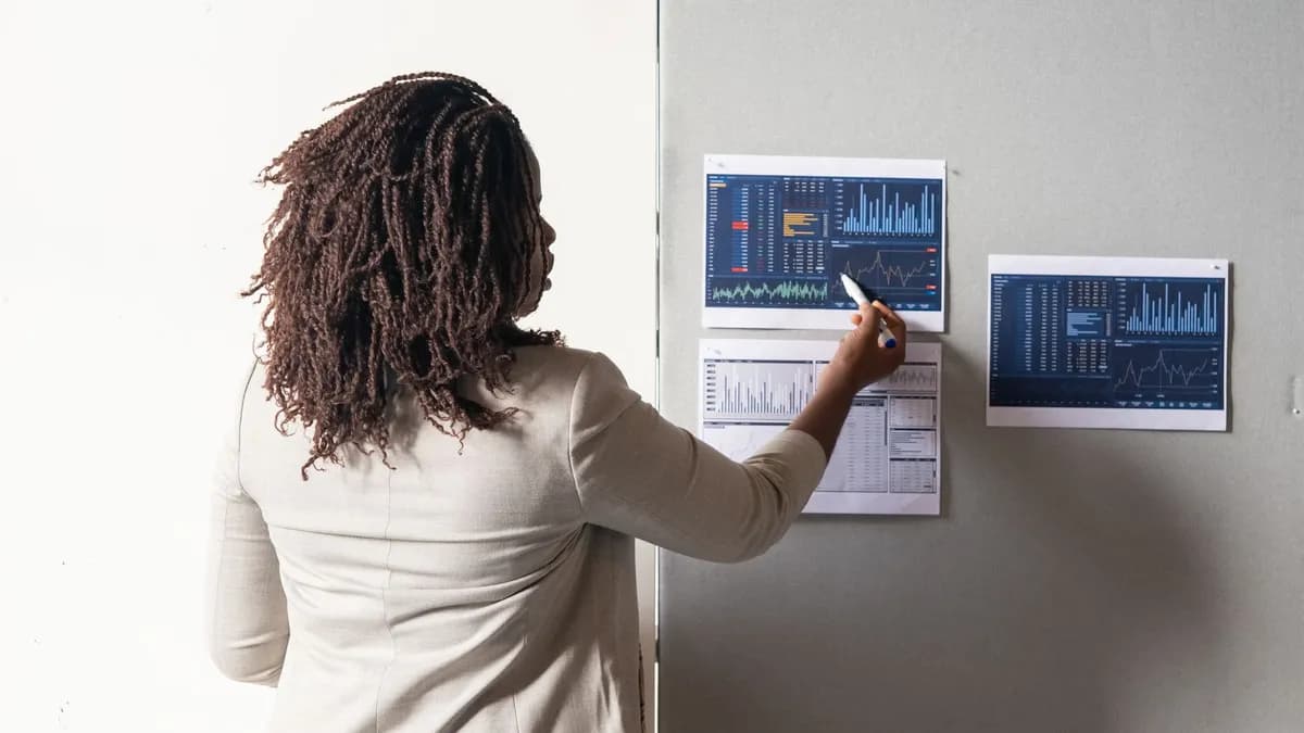 A businesswoman in a suit presenting financial data on charts during a meeting.