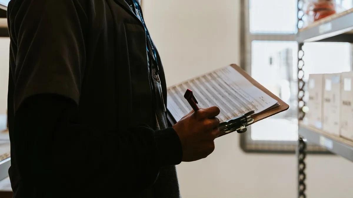 Industrial worker managing inventory in a warehouse with a clipboard and checklist.