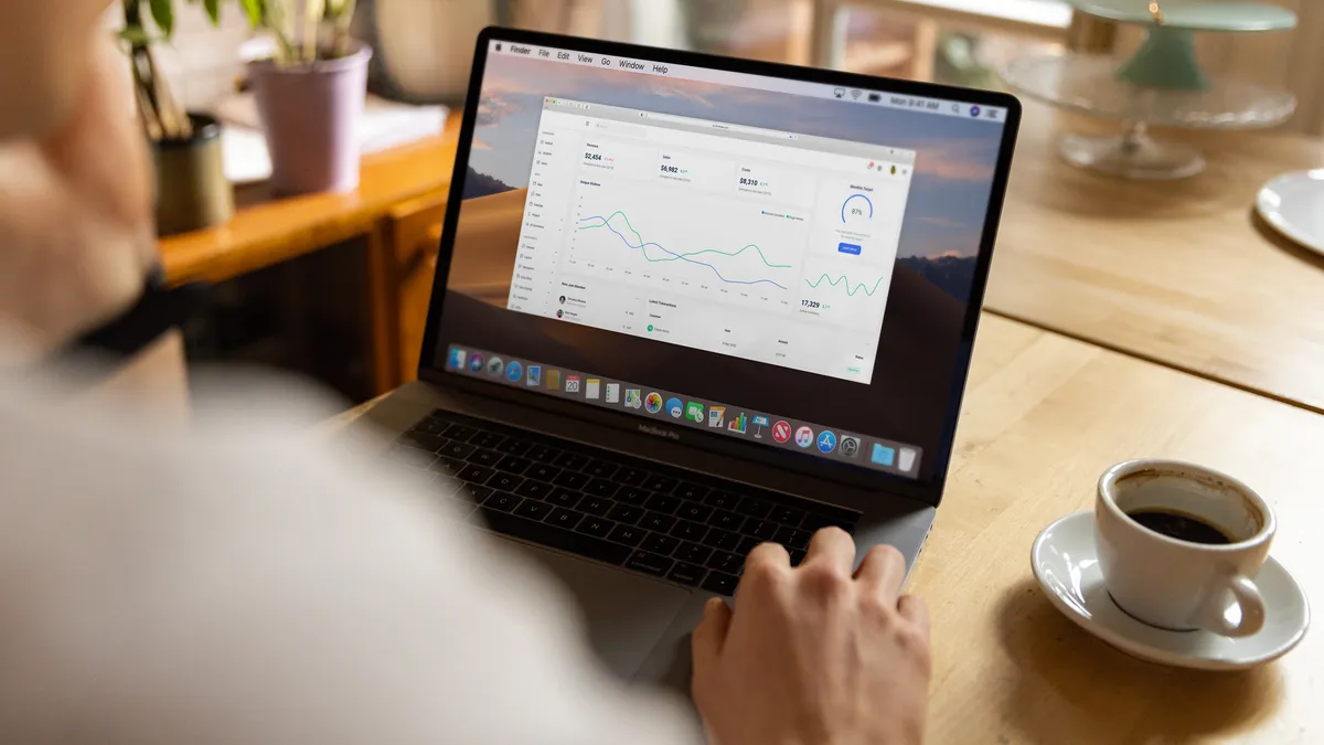 Person analyzing stock market data on laptop indoors with a casual setting and coffee.