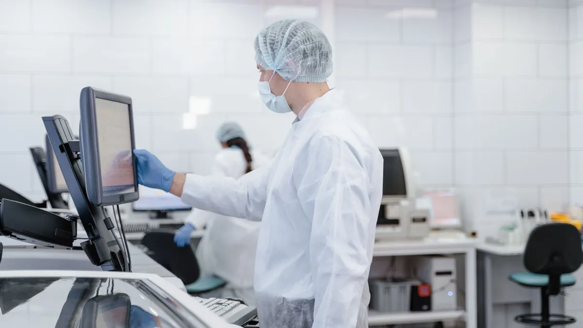 Scientist wearing protective gear while interacting with lab equipment and screen.