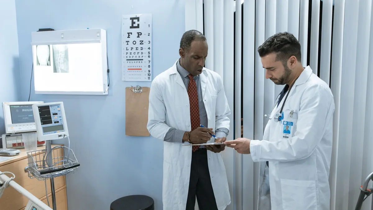 Two doctors in lab coats discussing a patient's medical chart in a hospital setting.