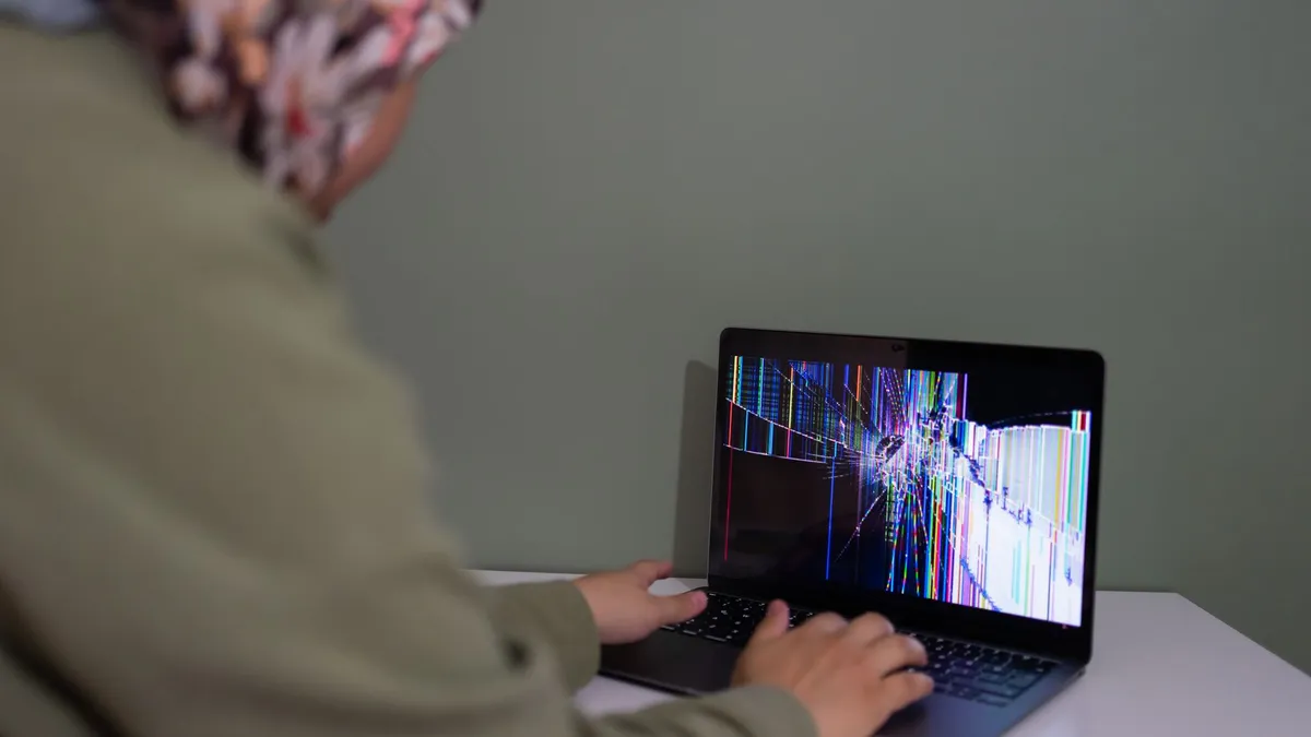 A person interacts with a laptop displaying a colorful cracked screen indoors.