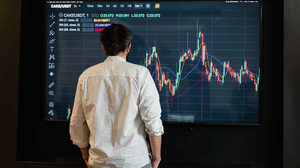 Back view of a trader analyzing cryptocurrency data on a monitor indoors.