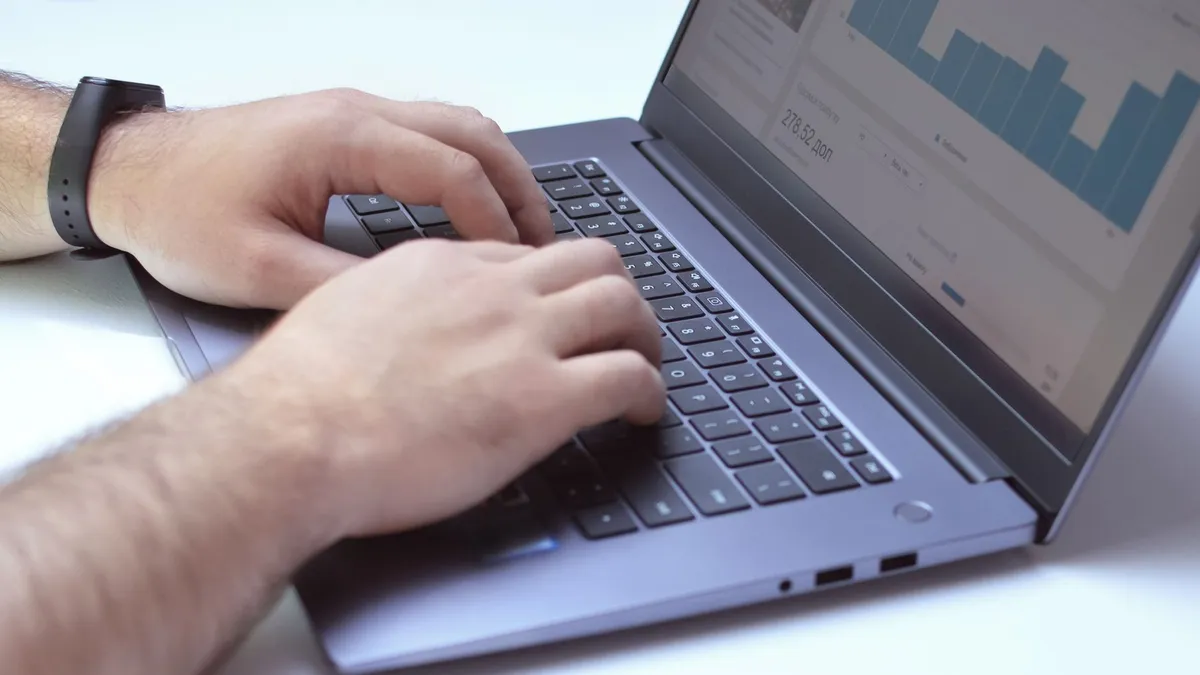 From above side view of crop unrecognizable male marketer working on netbook while using analytical software in office