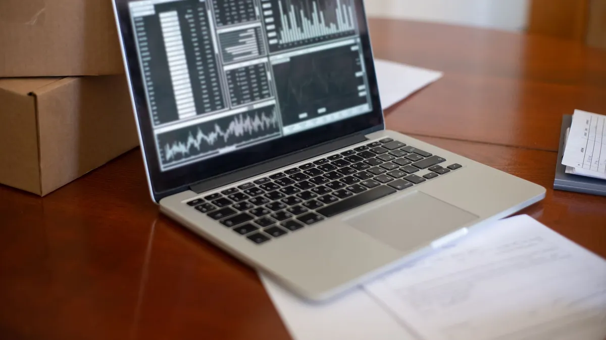 Laptop showing data graphs on wooden table with cardboard boxes, depicting a small business office setting.