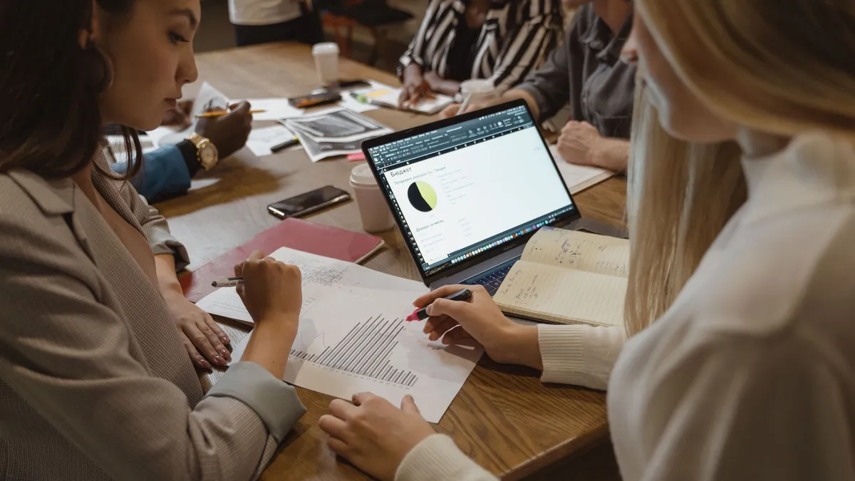 A diverse team collaborates on business strategy around a table with laptops and documents.