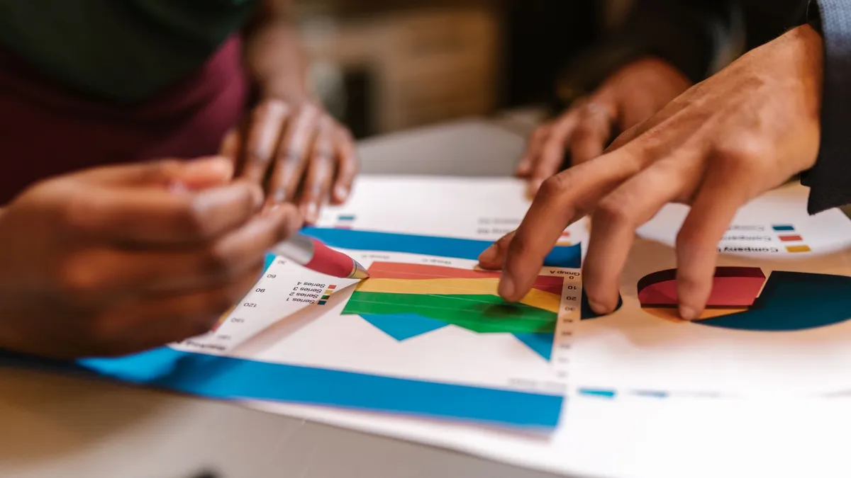 Close-up of hands during a collaborative office meeting analyzing colorful graphs and documents.