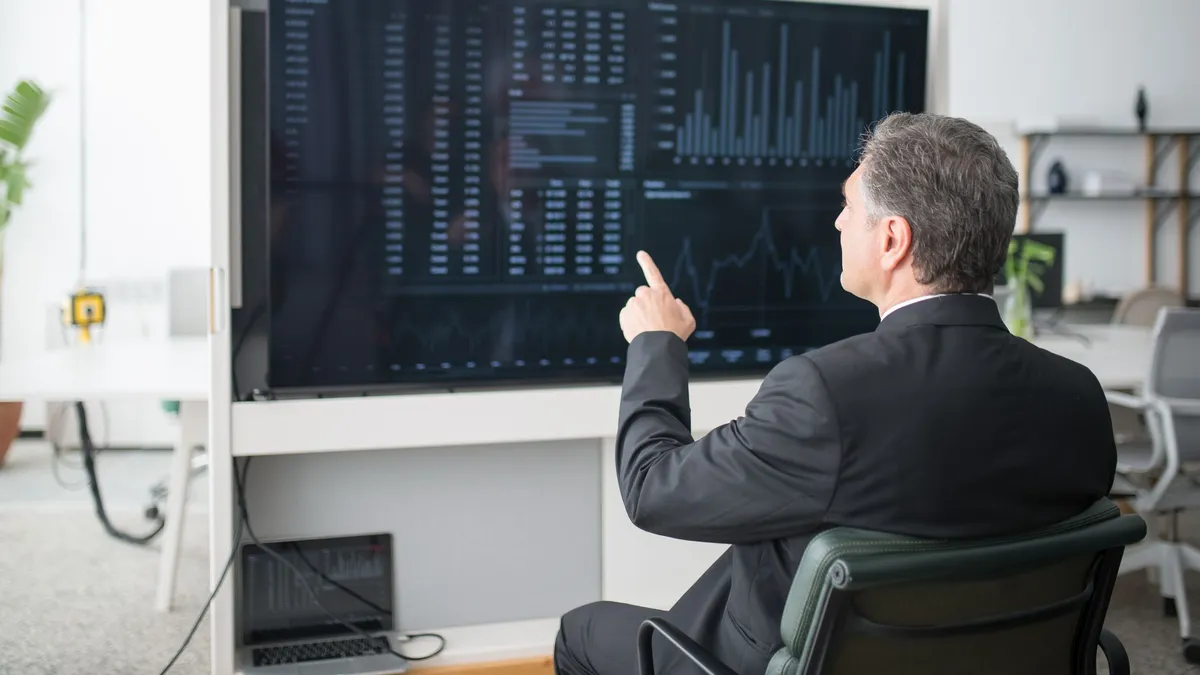 A businessman sitting and analyzing financial data on a large screen in an office.
