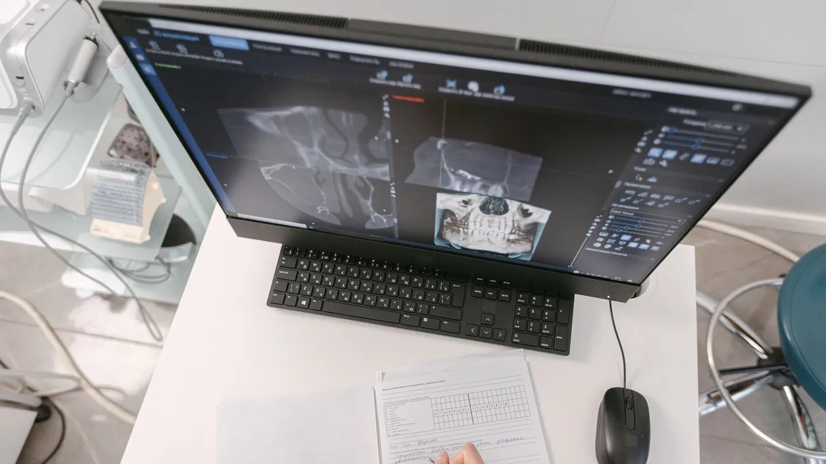 Radiologist analyzing X-ray scans on a computer monitor while taking notes. Medical documents visible.