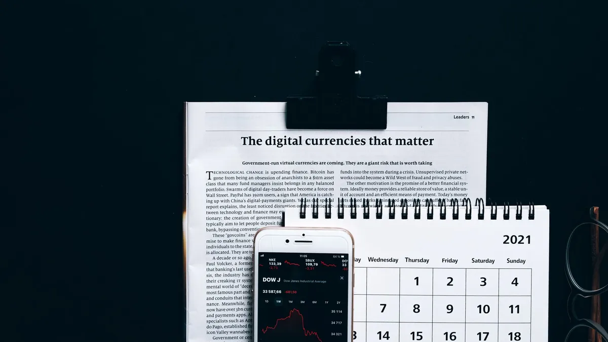 Digital currencies article with smartphone stock market app and calendar on black surface.