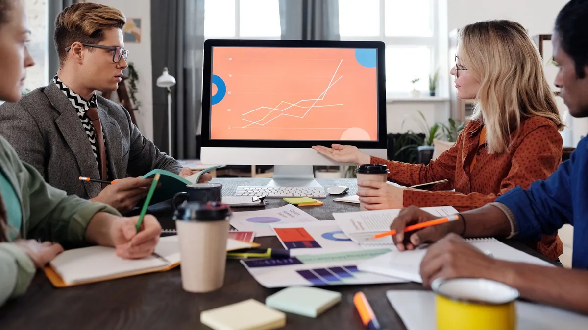 A diverse team discusses data visualization on a computer screen in an office setting.