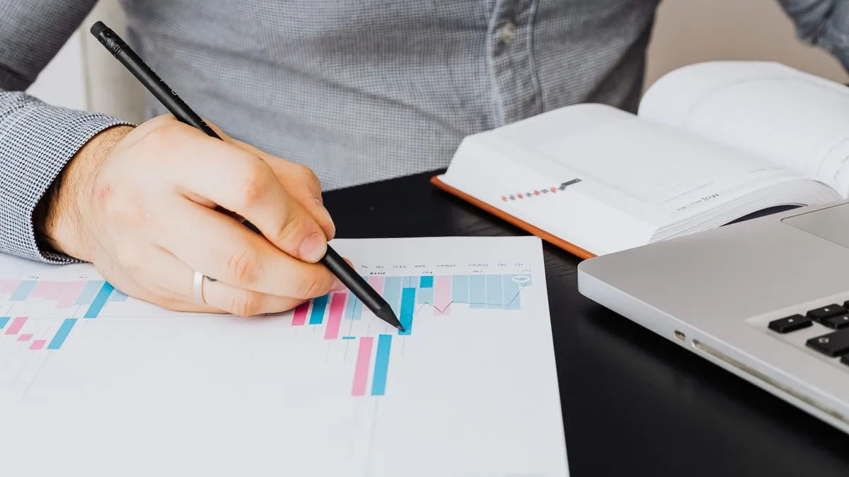 A business analyst examines a graph on paper with a laptop and notebook indoors.