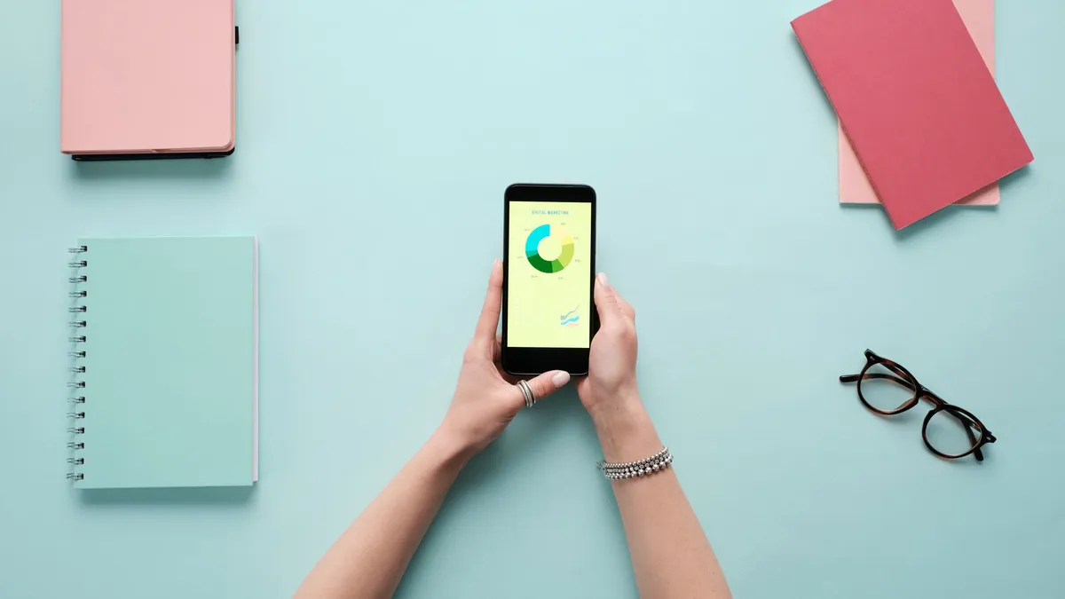 Overhead view of smartphone displaying business analytics on a vibrant blue background with stationery items.