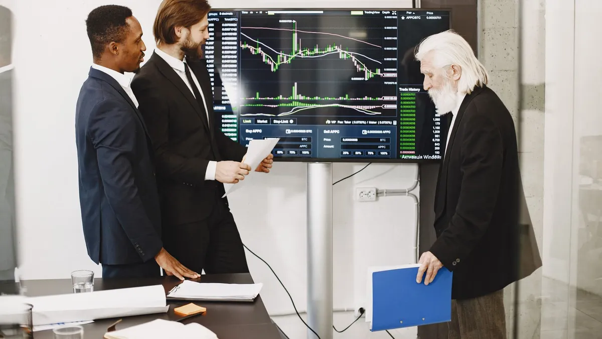Three businessmen analyzing financial charts on a screen in an office setting.