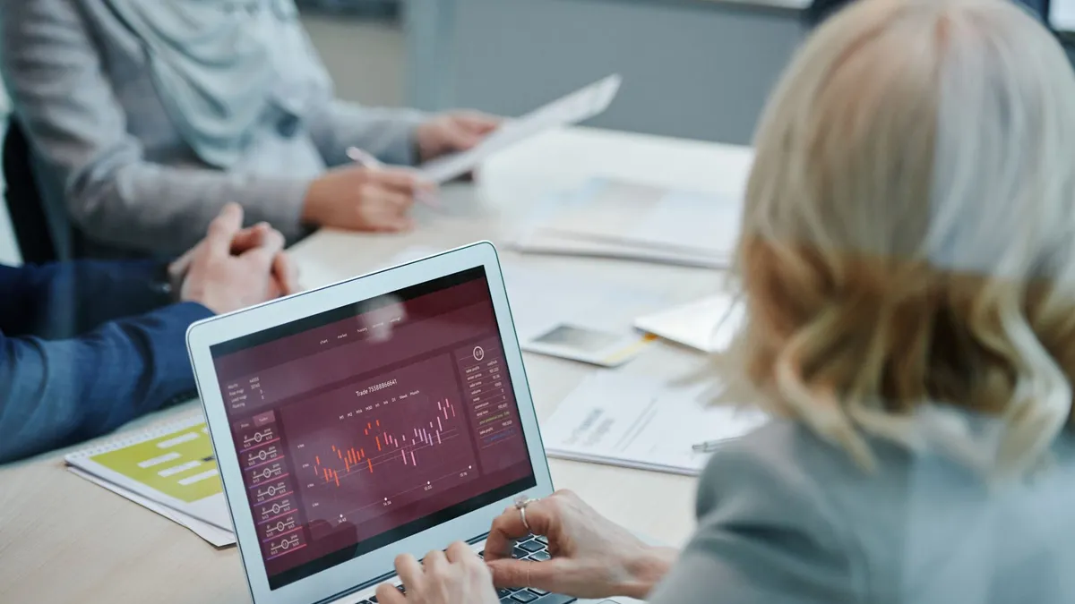 Business professionals analyzing stock market data on a laptop during a meeting.