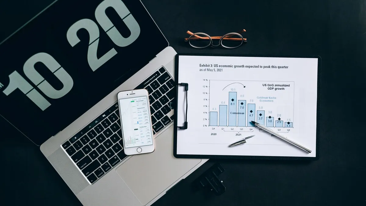 Top view of financial analysis tools on a desk including a laptop, smartphone, and graphs.