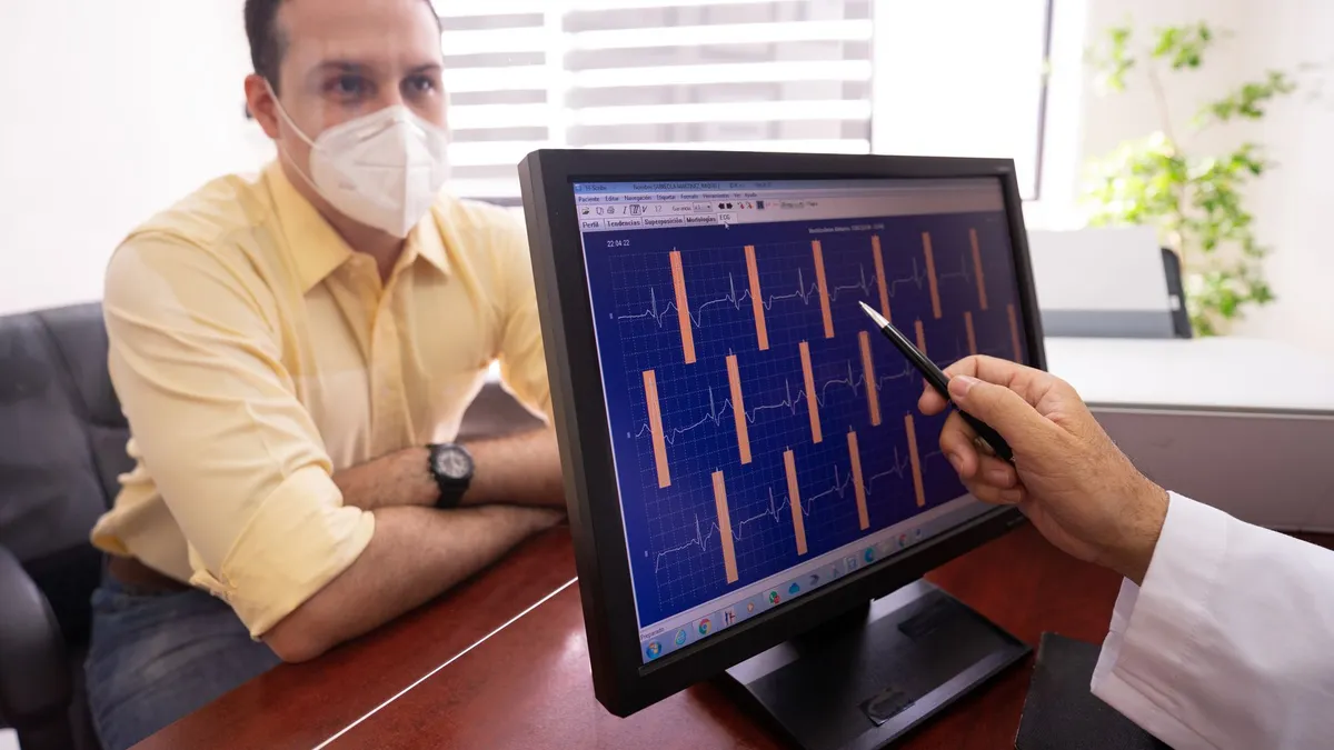 Medical consultation as a doctor reviews ECG results with a masked patient in a clinic setting.