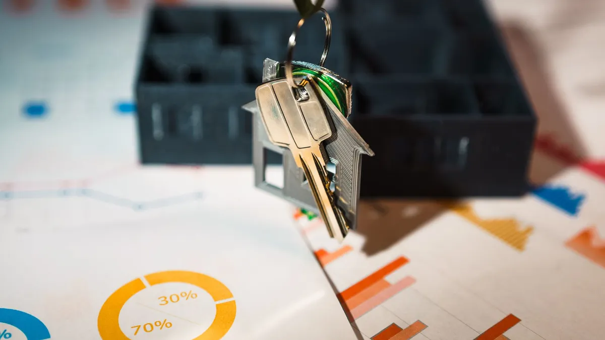 Real estate keys on house keychain with financial graphs, symbolizing property investment.