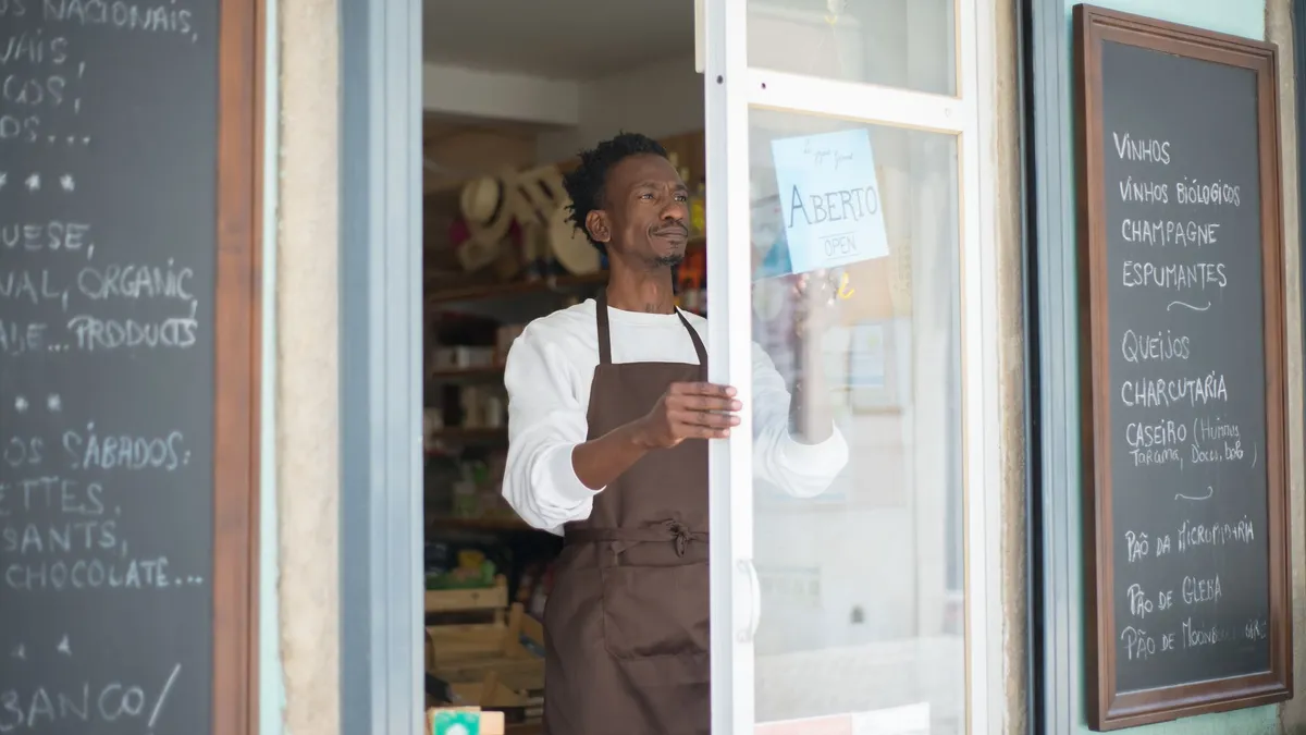 A man in an apron opens a grocery store door in Portugal, ready for business.