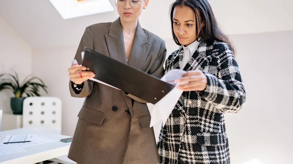 Two businesswomen reviewing documents in a modern office setting.
