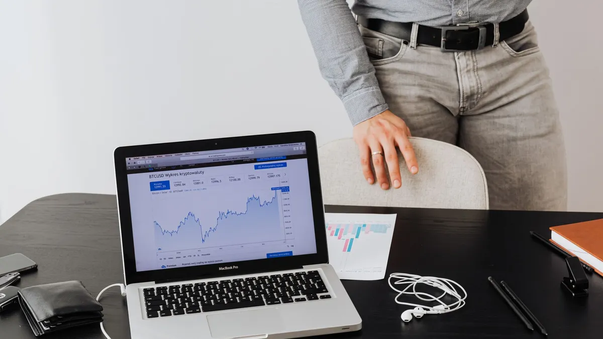 A businessman stands next to a laptop displaying cryptocurrency data, symbolizing modern digital finance.