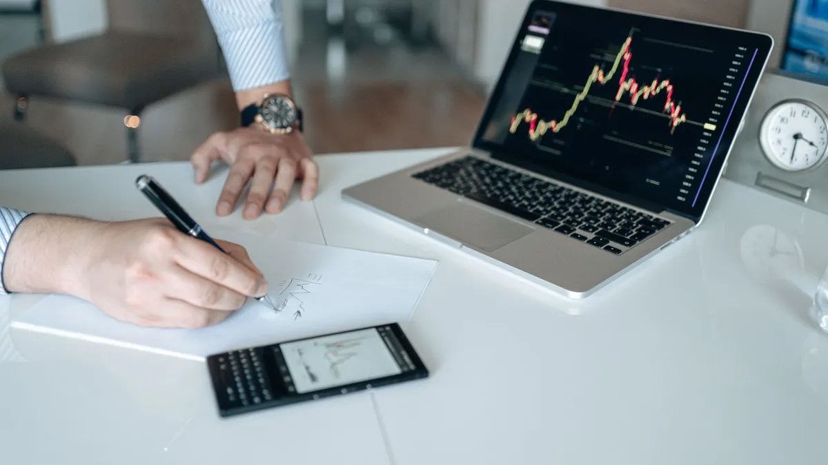 Professional workspace with a laptop displaying financial graphs and a person writing.