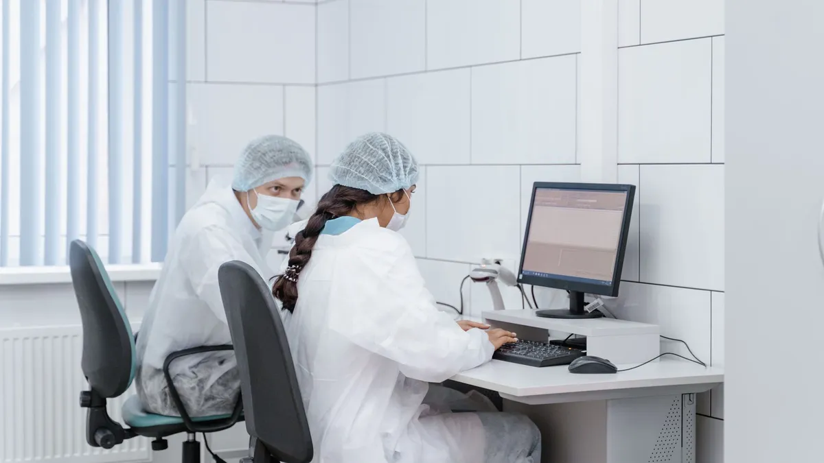 Two scientists at a computer in a laboratory setting, analyzing data with focus and precision.