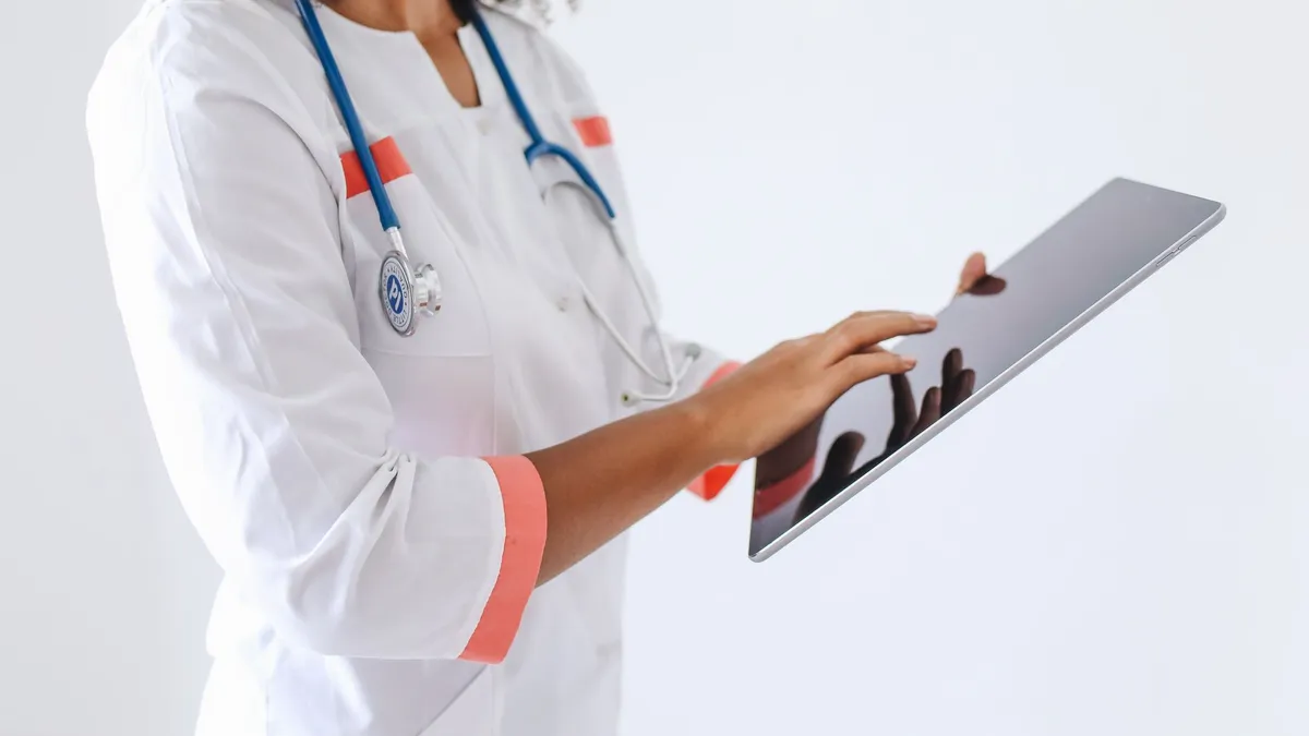 A doctor wearing a face mask and stethoscope using a tablet in a medical setting.