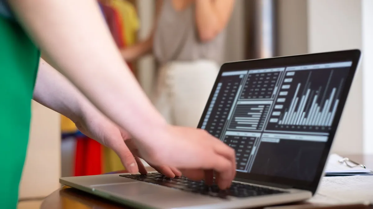 Hands typing on a laptop displaying data charts in an indoor setting.