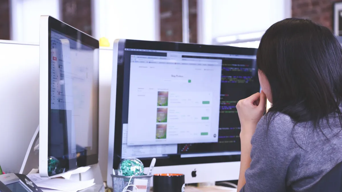 Professional woman focused on work using dual monitors in a modern office.