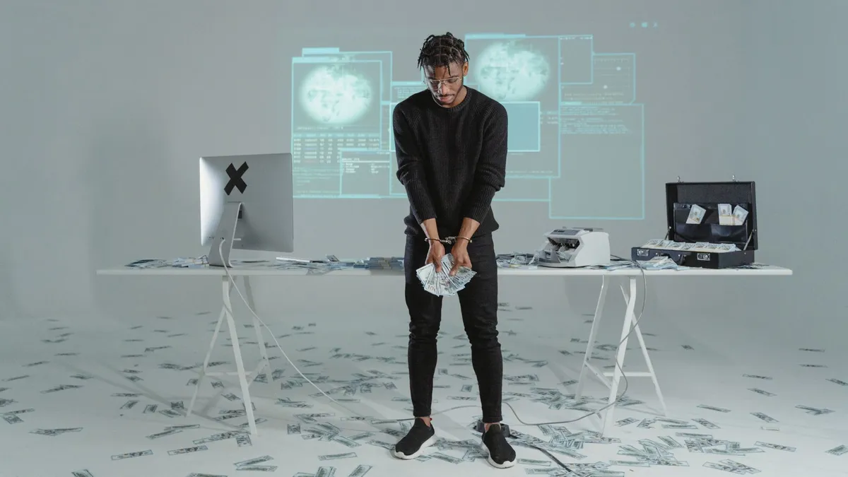 A man stands holding money in a high-tech room with scattered bills and a computer setup.