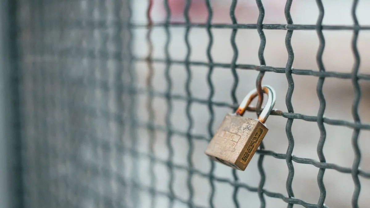 Small iron lock hanging on rusty metal grid for protection and safety of private area
