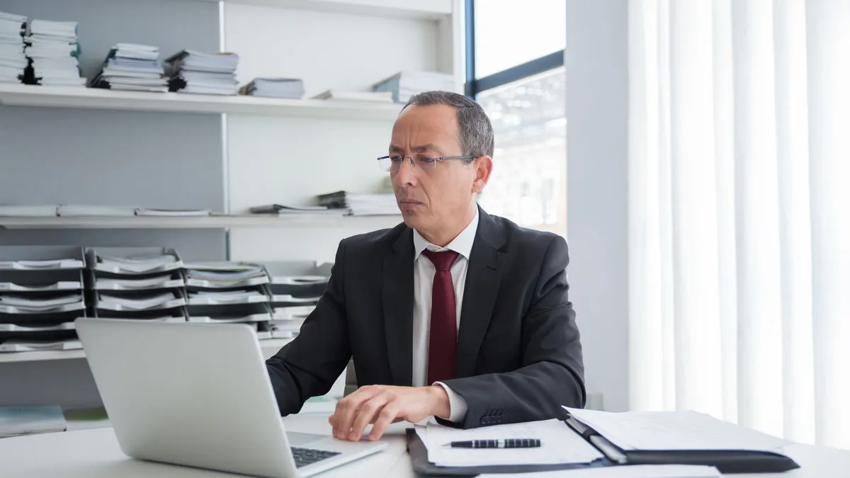 Focused businessman in a suit working at his office desk with a laptop and documents.