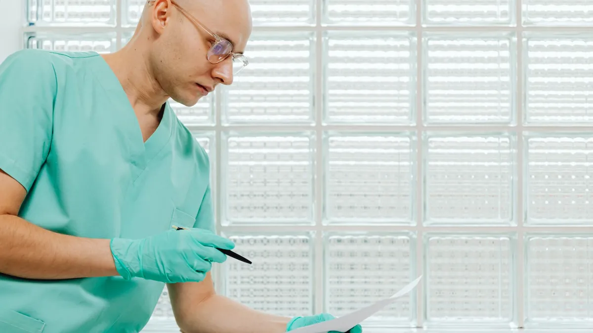 A healthcare worker in scrubs and gloves examines a document with focus.