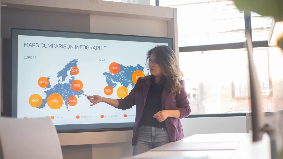 A professional woman presents an infographic comparing Europe and Asia in a bright, modern office setting.