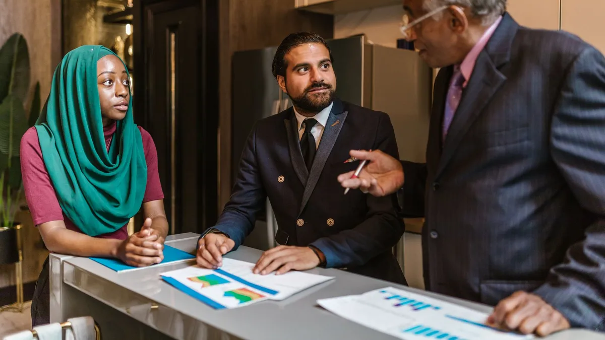 Three business professionals engage in a discussion, showcasing diversity and teamwork in a modern office setting.