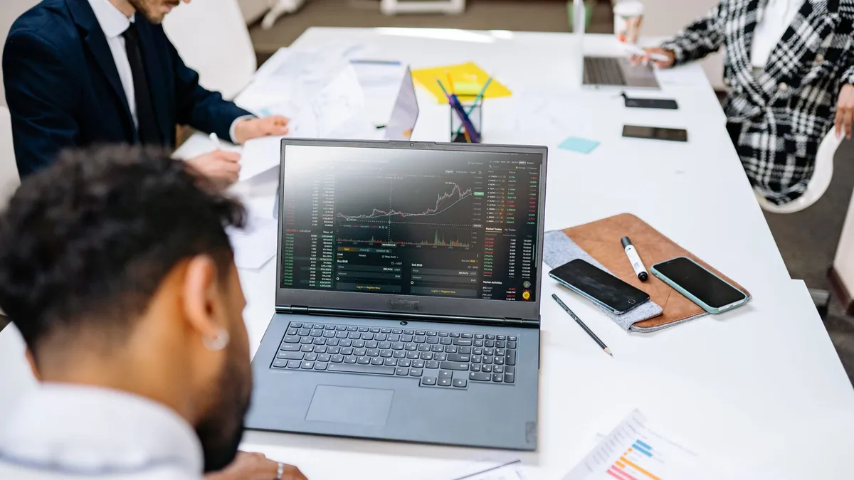 Team collaborating in an office setting, discussing financial graphs on a laptop screen.