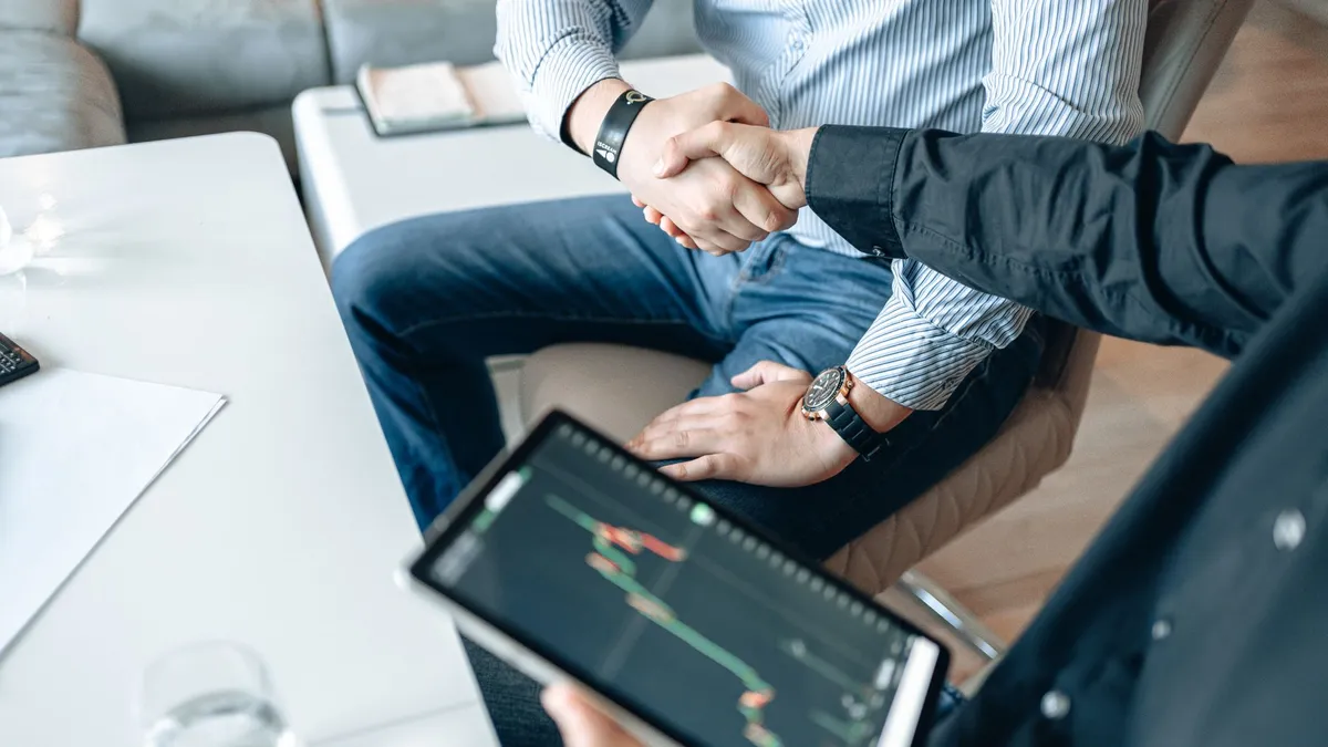 Business professionals shaking hands with a tablet displaying financial graphs.