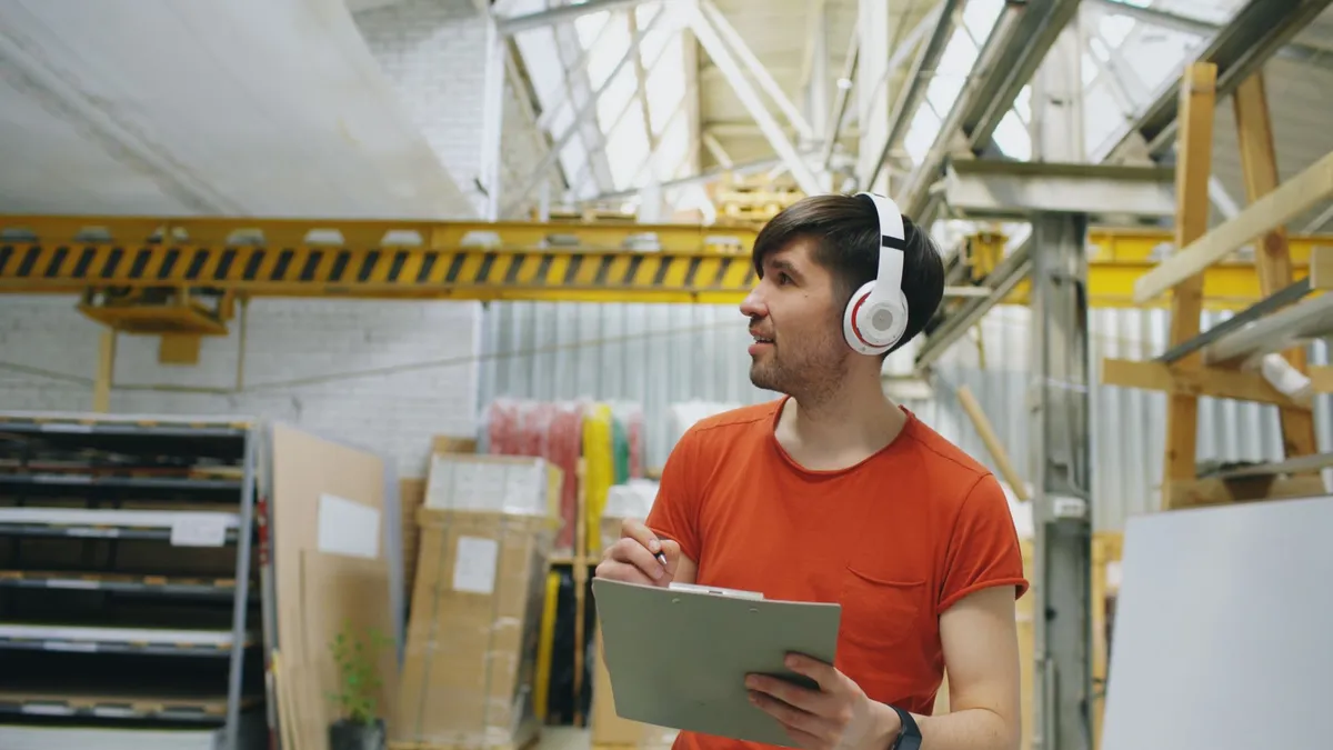 Young adult warehouse worker wearing headphones while taking inventory indoors.