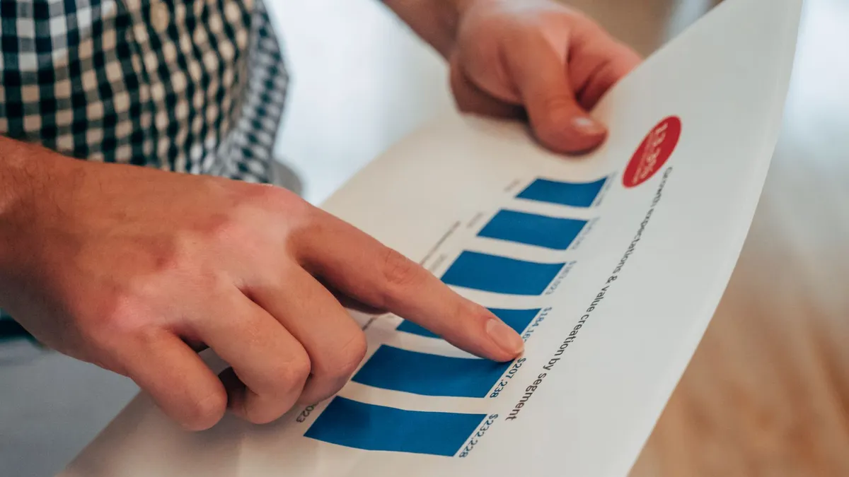 Close-up of hands pointing at a bar chart on paper, analyzing financial stats and report.