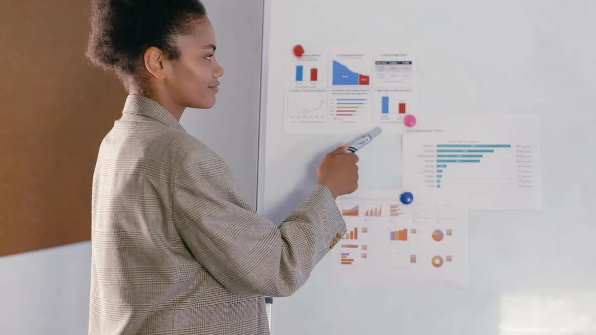 Professional woman in a blazer discusses finance graphs on a whiteboard during a presentation.